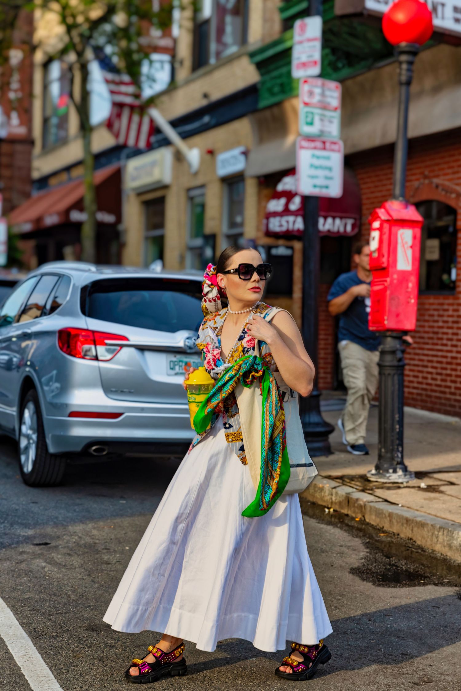 White summer dress styled with colorful scarf and sandals on city sidewalk.