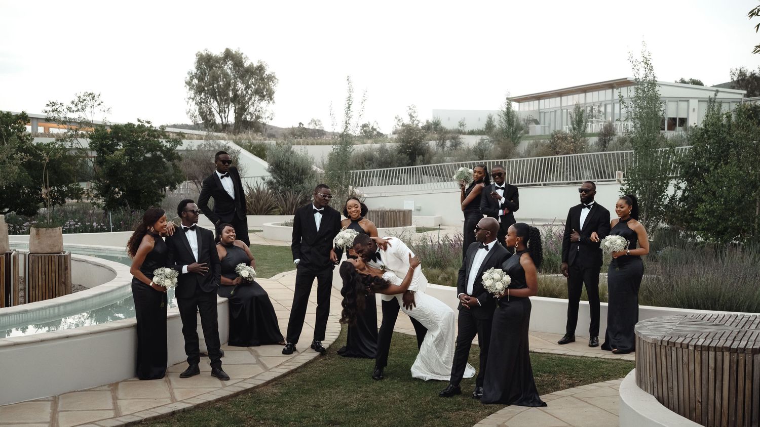 A panoramic view of wedding guests gathering outdoors near a waterfront venue on an overcast day.