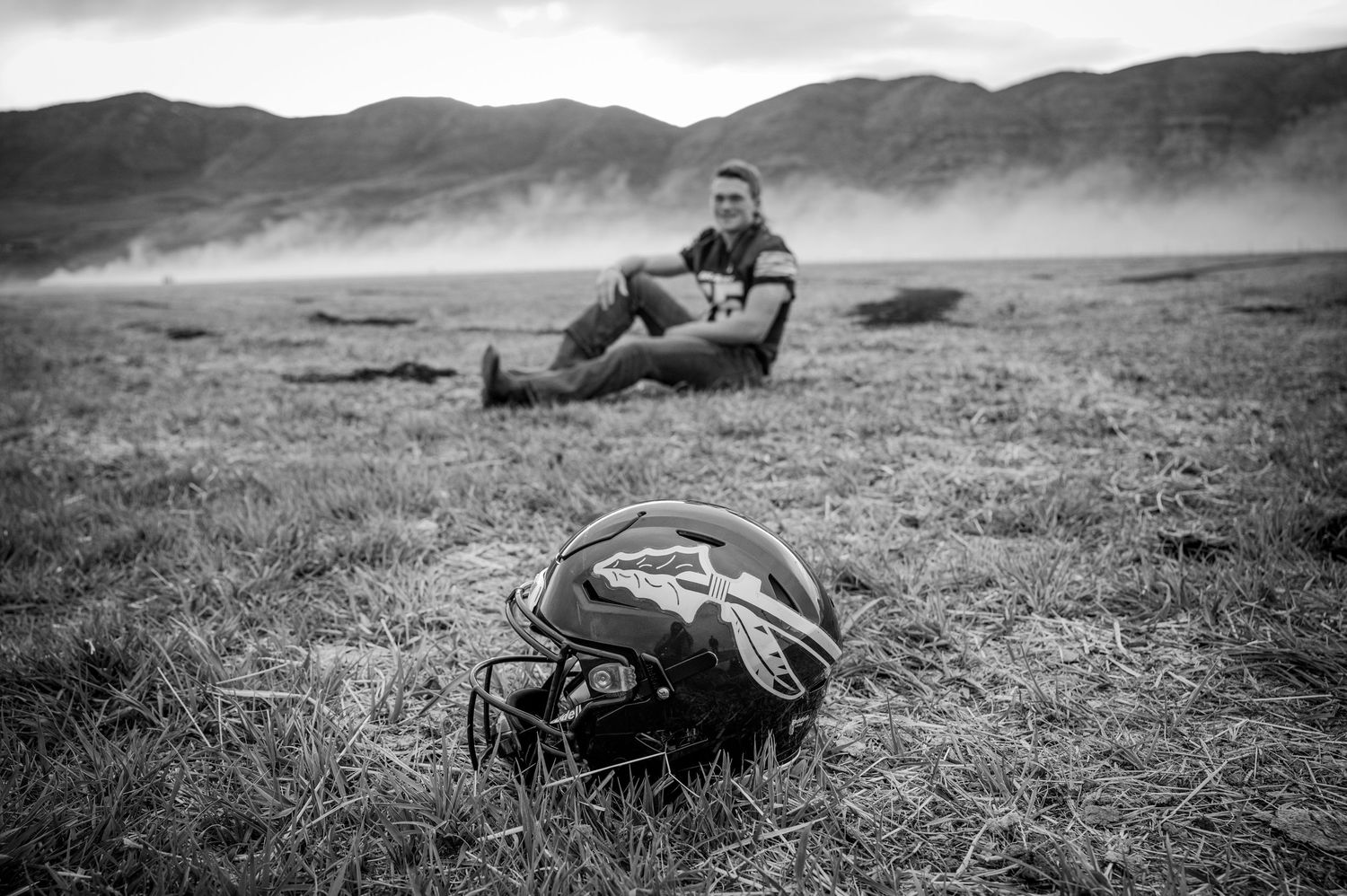 Black and white photo of motorcycle gear on rugged terrain with mountains in background.