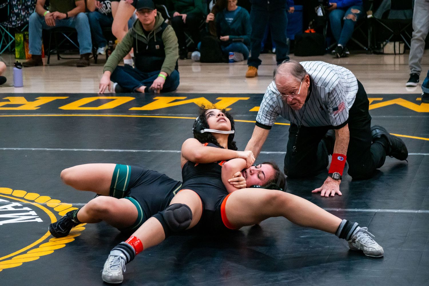 Wrestling match sequence showing athletes competing on dark mats with yellow markings.