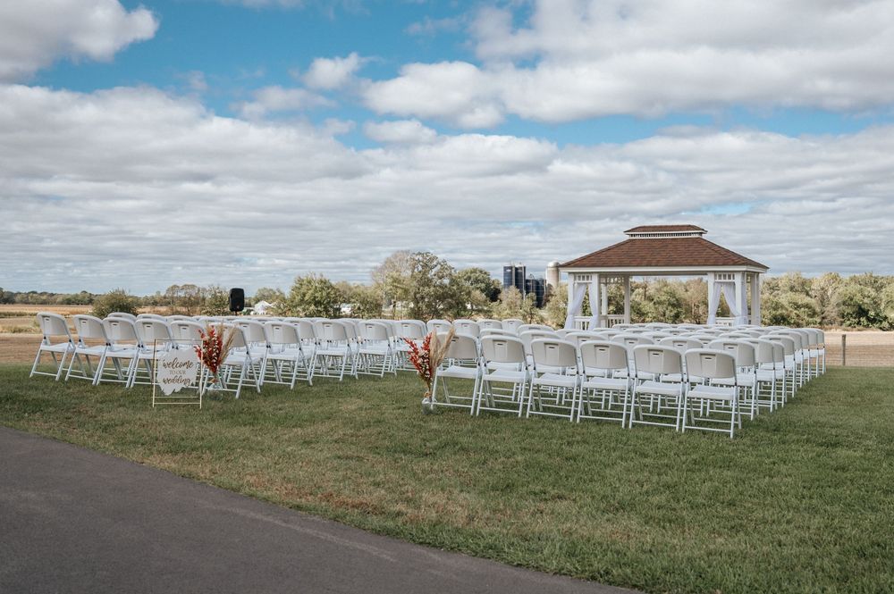 White wedding chairs arranged in rows on a grassy hill with a scenic countryside backdrop.