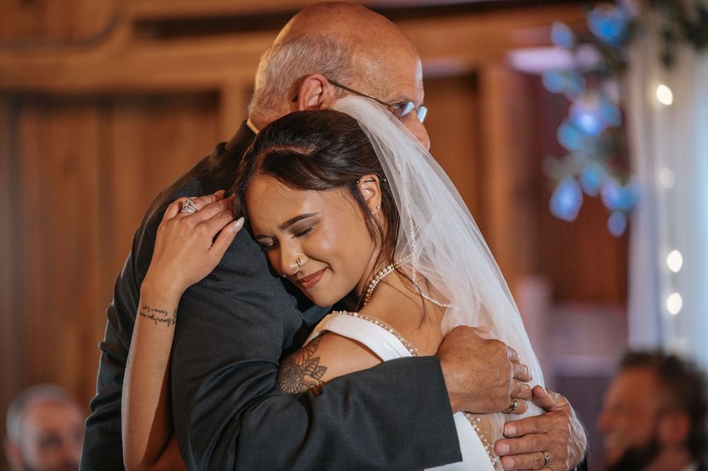 An emotional embrace during a wedding celebration inside a warmly lit wooden barn venue.
