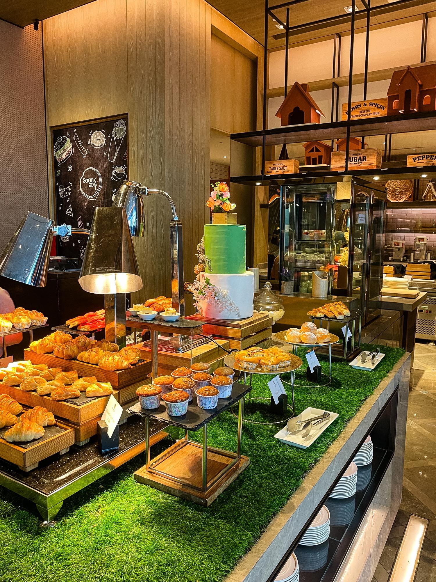 Fresh bread and pastries displayed on wooden crates with artificial grass in a modern bakery setting.