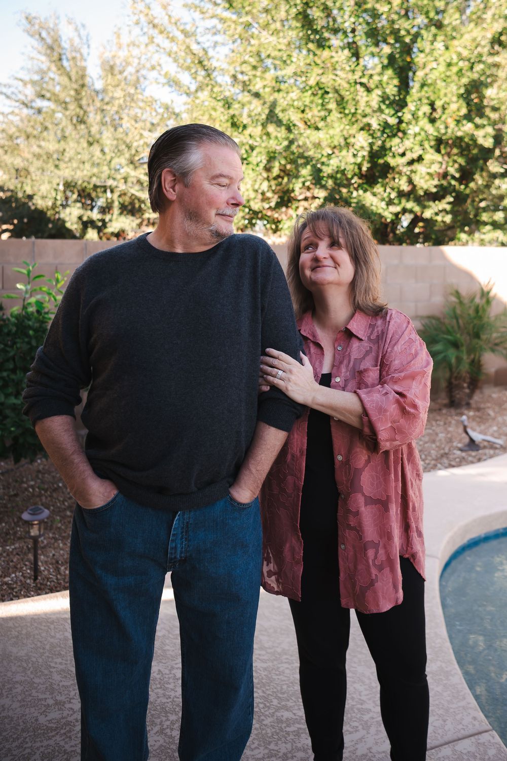 A couple shares a tender moment outdoors by a pool on a sunny autumn day.