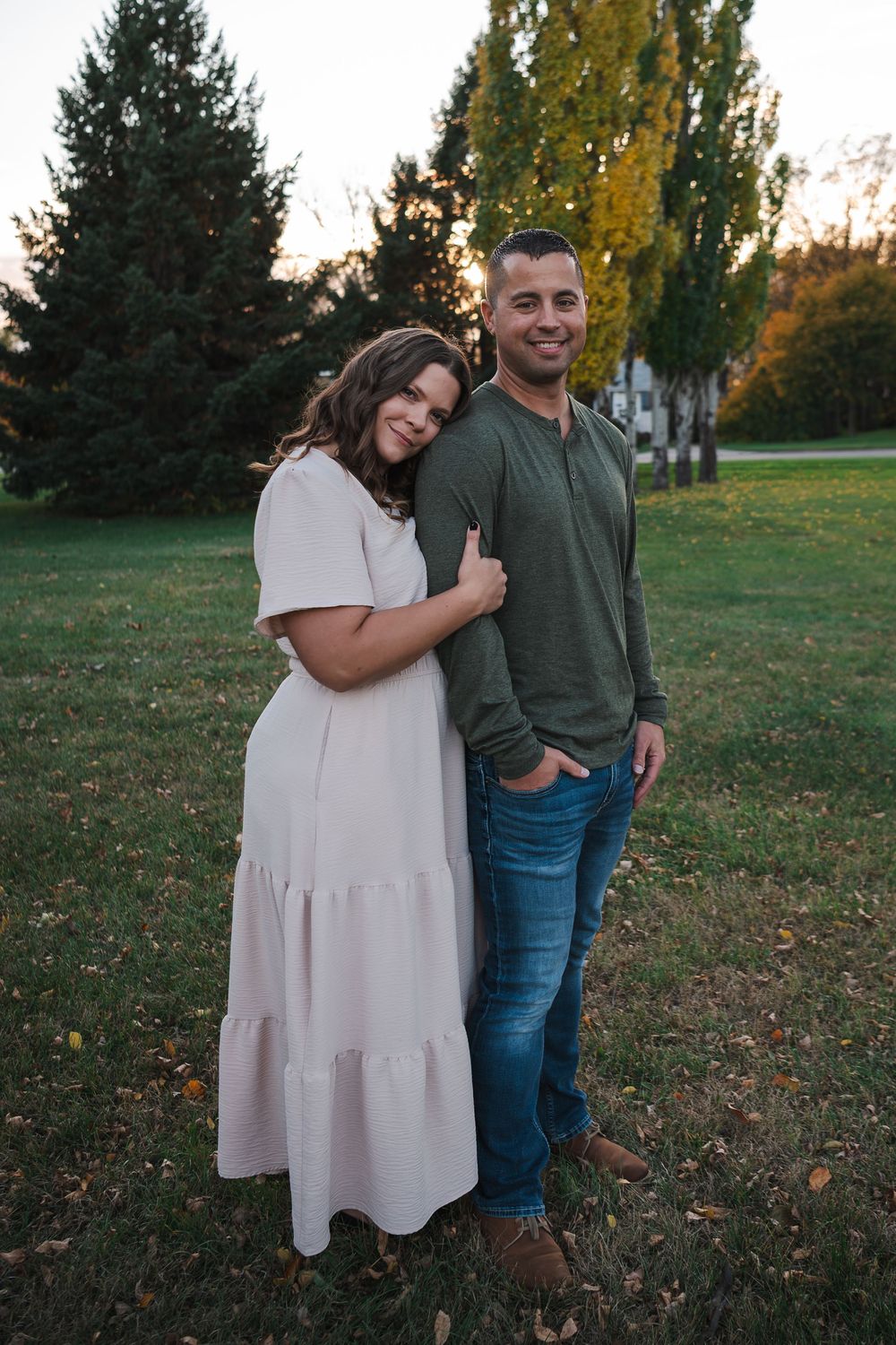 Couple in casual attire poses together in a park during autumn.