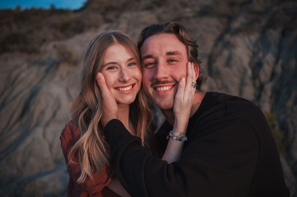 A couple shares an intimate moment against a dramatic rocky backdrop at sunset.