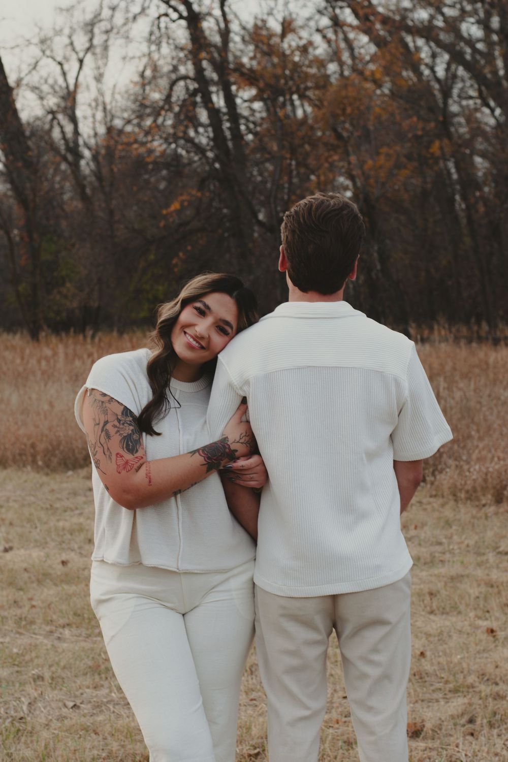 A couple wearing matching white outfits embraces in an autumn field.