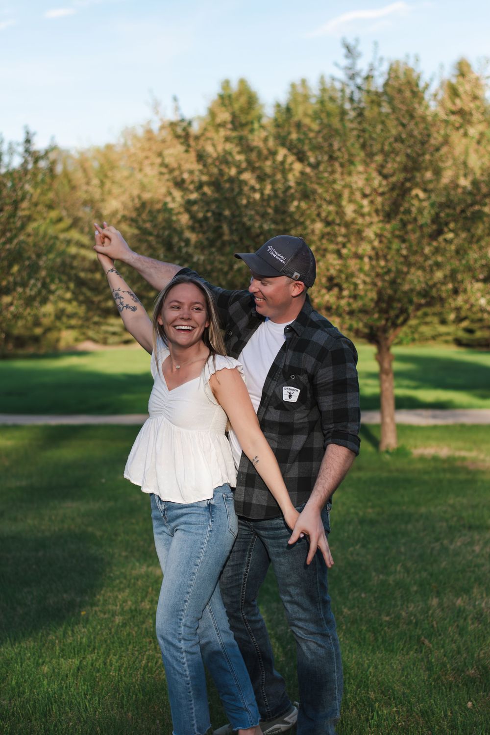 A joyful couple dances together in a sunny park with trees in the background.