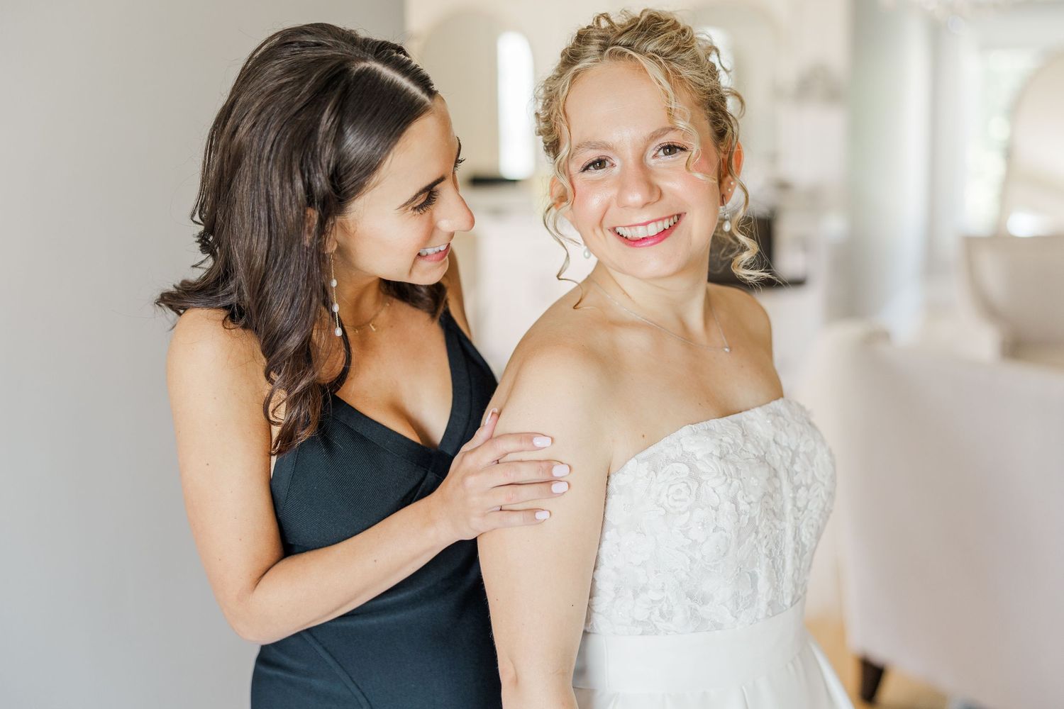 Bride in white dress and bridesmaid in navy share an intimate moment during wedding preparations.