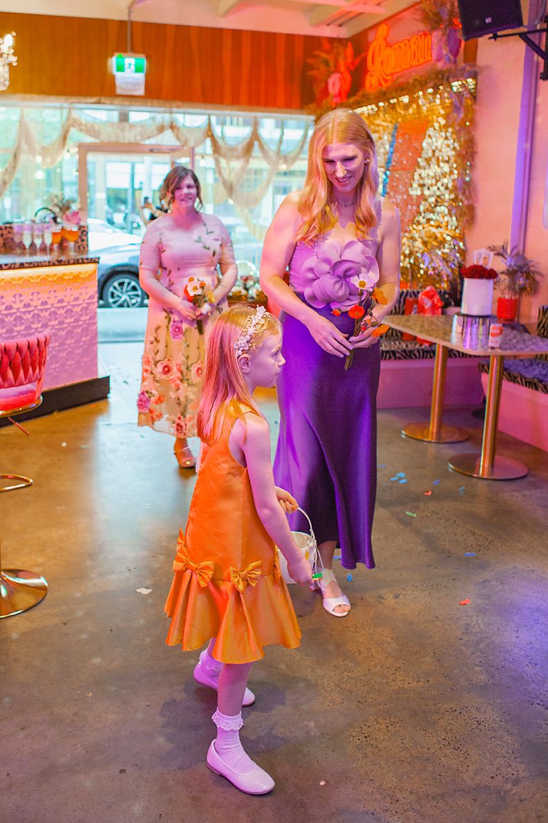 Dancers in orange and purple dresses perform a coordinated dance routine in a festively decorated venue.