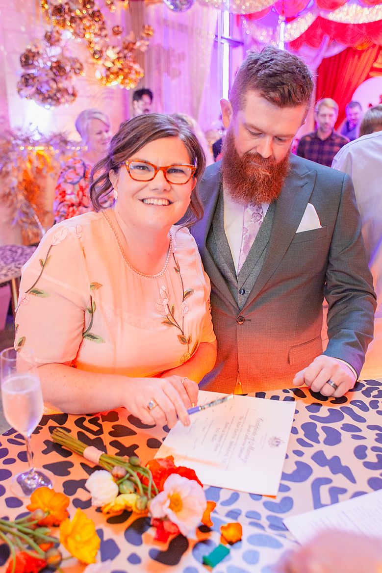 A couple signing documents at a table decorated with colorful flowers during a wedding ceremony.