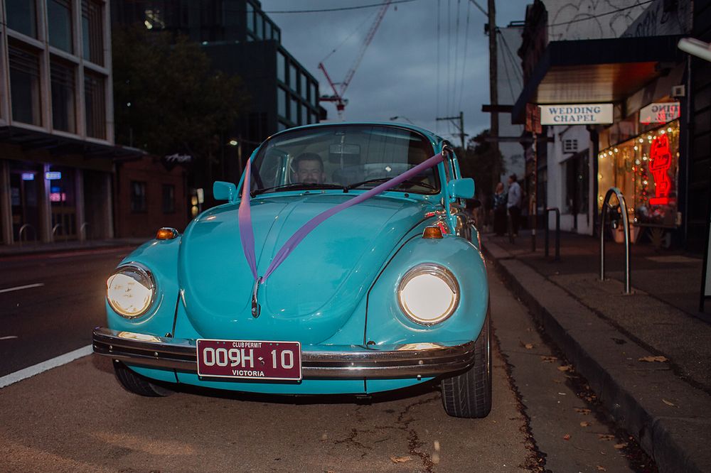 A classic turquoise Volkswagen Beetle car parked on a city street at night.