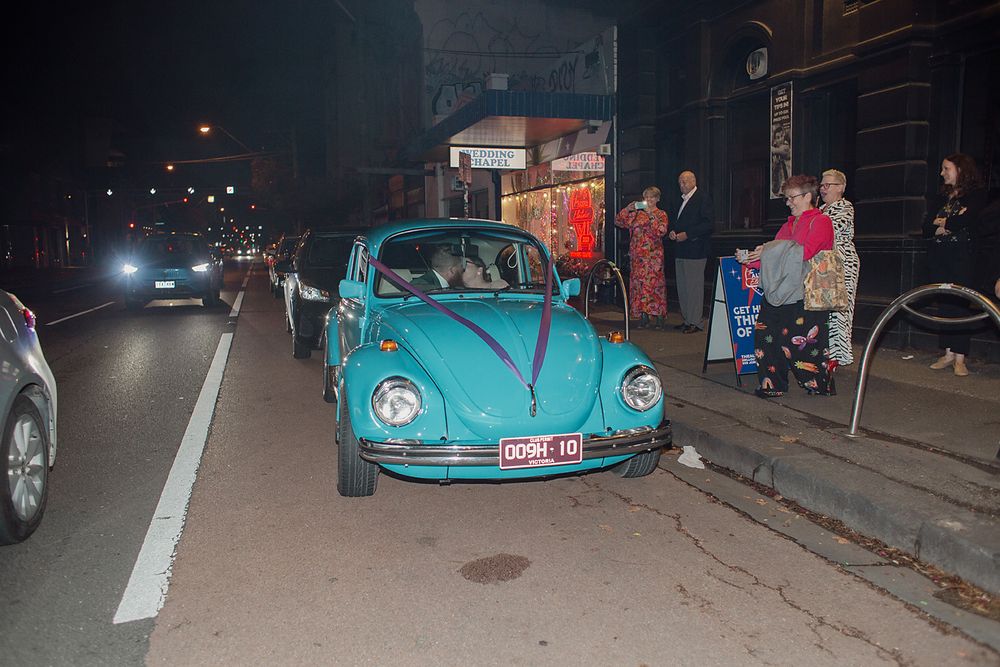 A row of classic Volkswagen Beetles in turquoise blue color parked at a nighttime car show event.