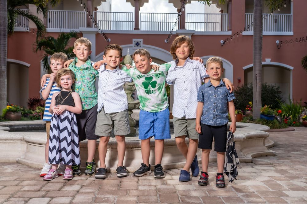 Row of children's legs and feet dangling from a bench against a brick building background.