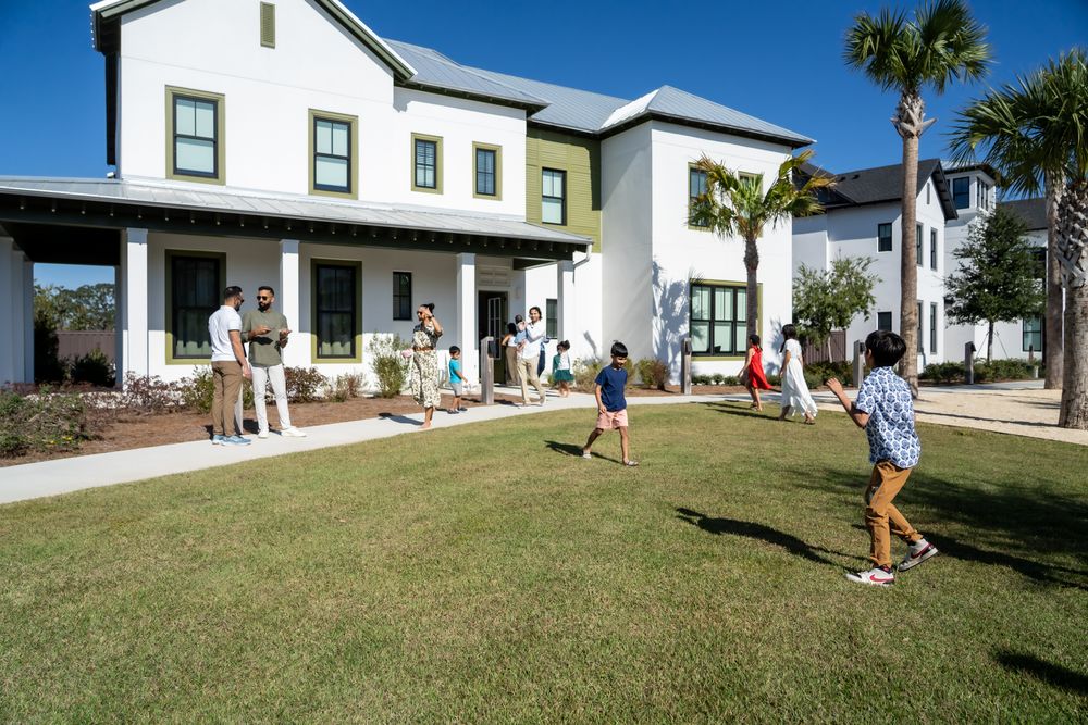 People enjoying outdoor activities on a green lawn in front of white coastal-style homes with palm trees in Florida.