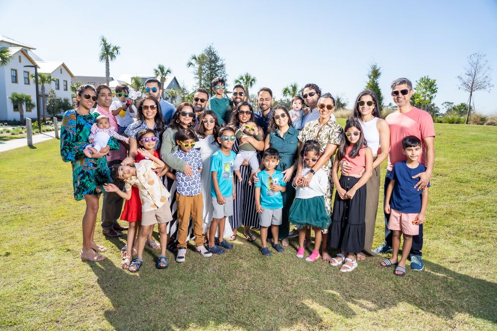 Large group of people gathered outdoors on sunny day with palm trees and houses in background.