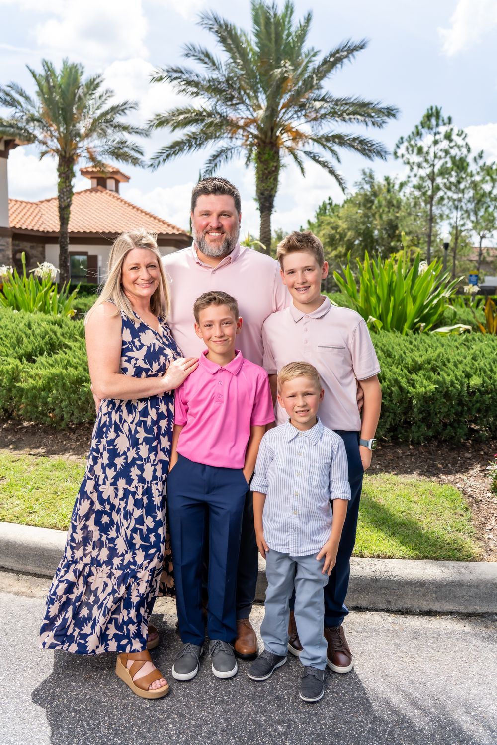 A family of four poses outdoors together in front of tropical landscaping and palm trees.