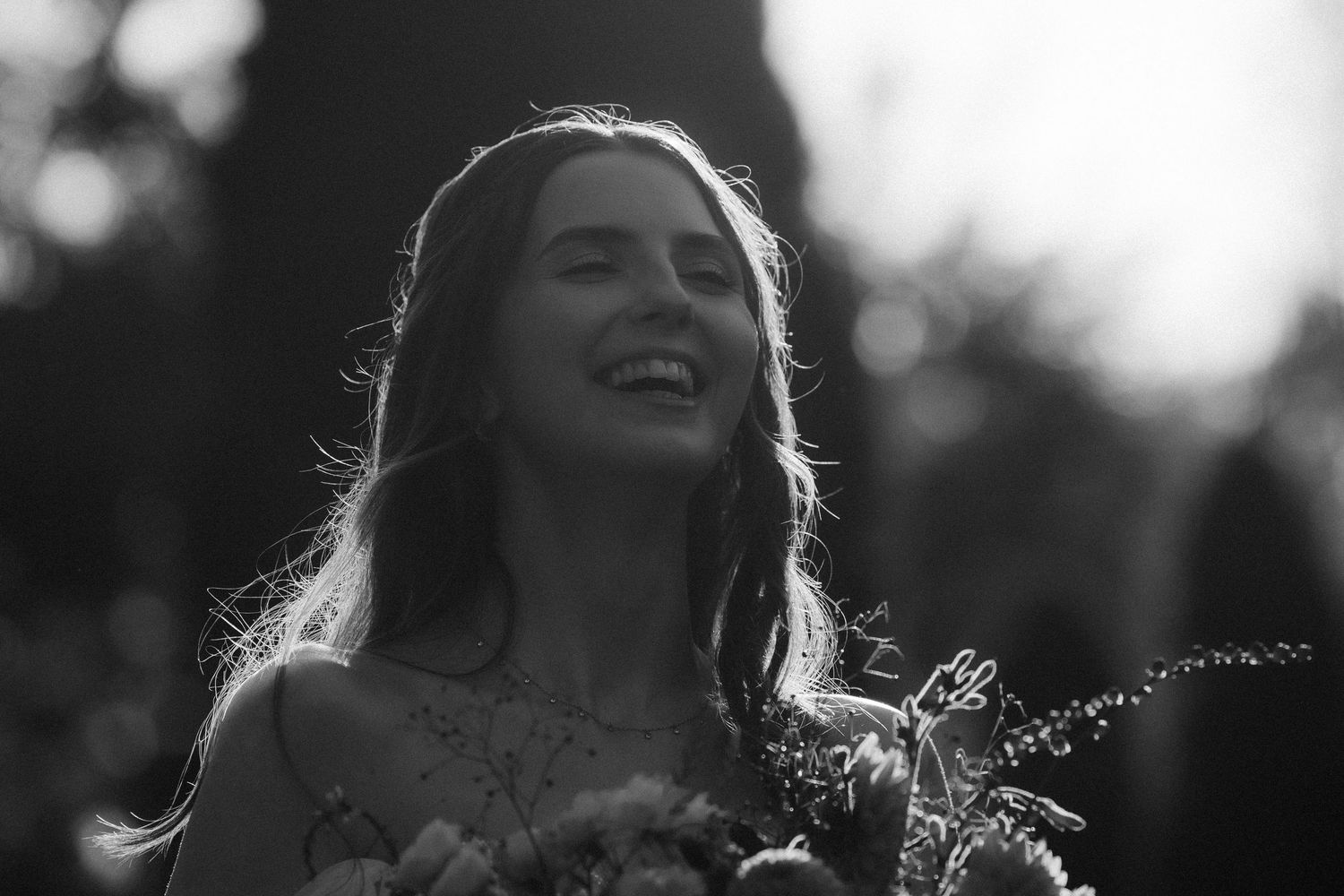 A person laughs joyfully with their head tilted back while standing in natural light outdoors.