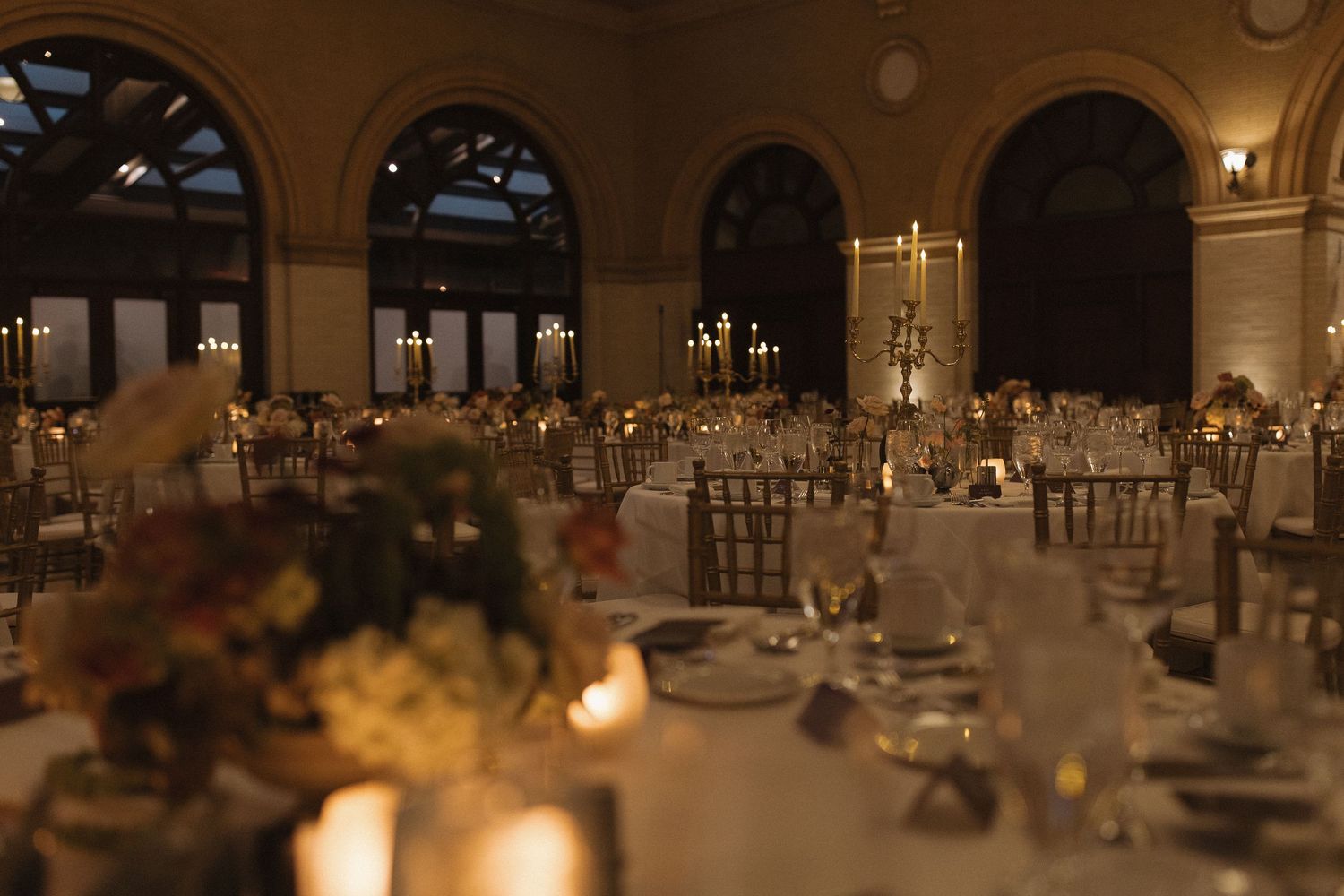 Elegant wedding reception ballroom with crystal chandeliers, white floral centerpieces, and candlelit tables set for dinner.