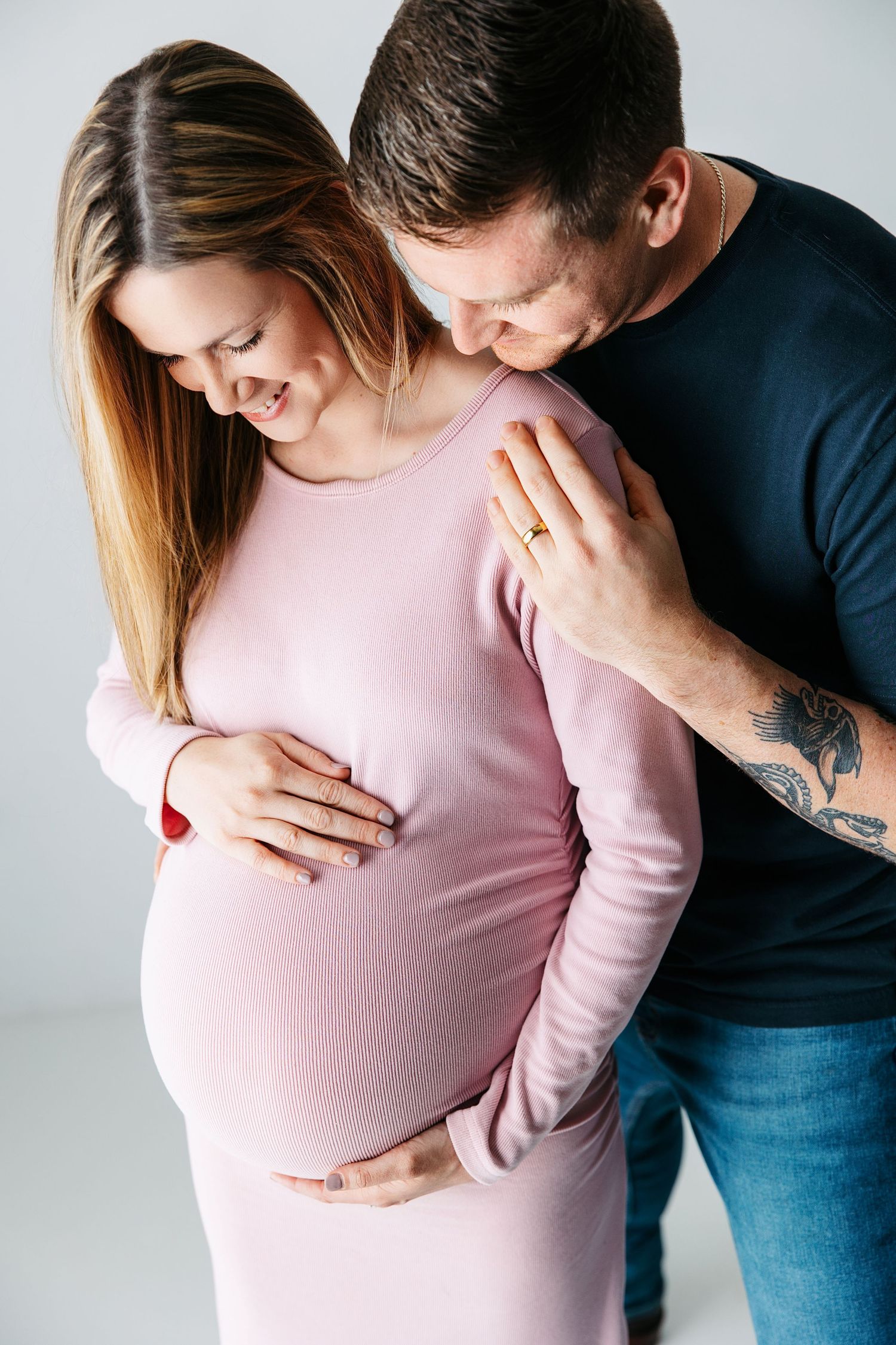 Expectant parents share intimate moments while celebrating pregnancy in a minimalist studio setting. Pleasant View maternity photographer