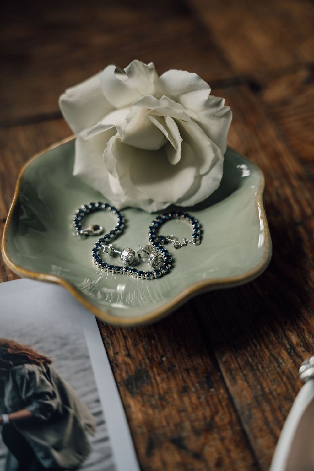 White rose and delicate jewelry displayed on mint green ceramic dish with gold trim.