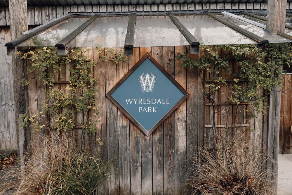 Rustic wooden entrance sign for Wyresdale Park with climbing vines and greenery.