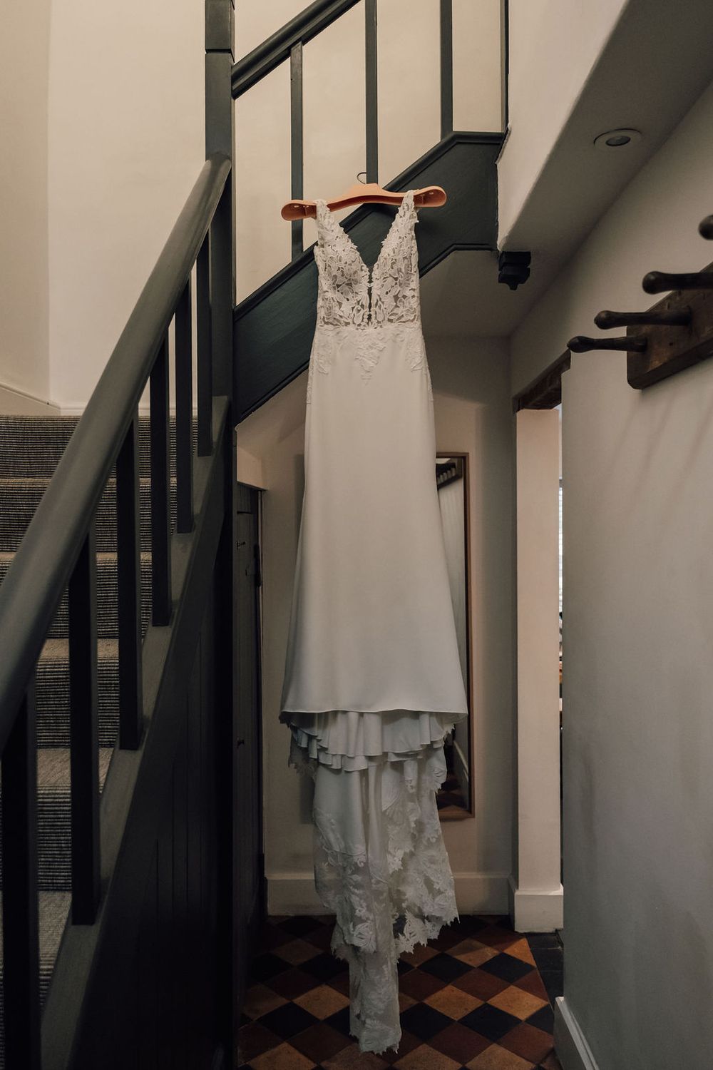 Elegant white lace wedding dress hanging on staircase with detailed bodice.