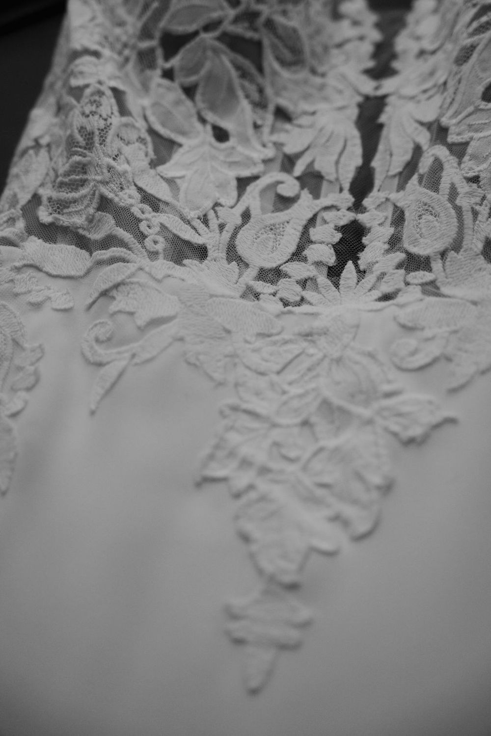 Close-up detail of intricate lace pattern on white wedding dress fabric.