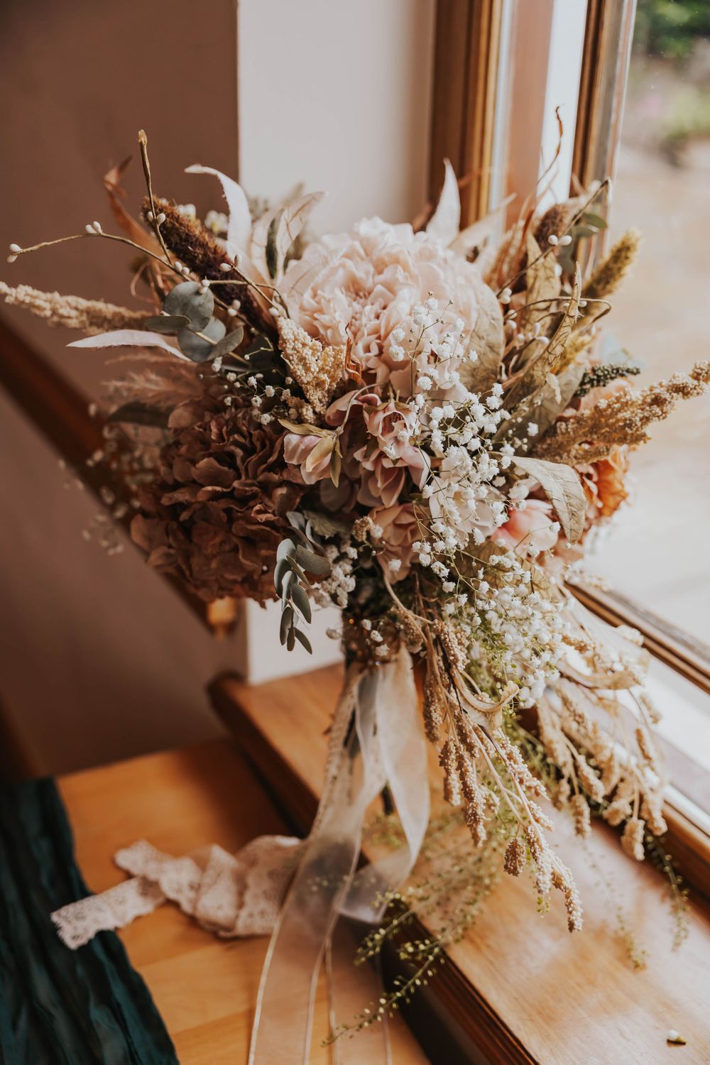 A series of dried flower arrangements with pampas grass and white blooms displayed on wooden windowsills in warm lighting.