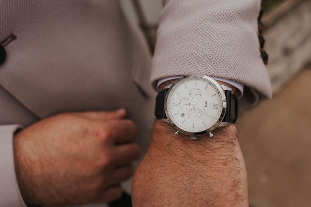 Close-up of a classic white-faced wristwatch worn with a beige suit sleeve.
