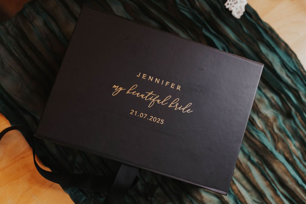 Elegant black invitation cards with gold foil lettering displayed on dark green palm leaves.