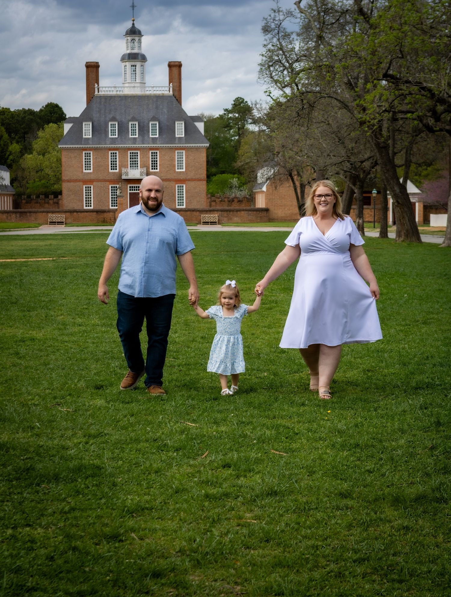 pregnancy announcement mom and dad holding oldest daughters hands walking in colonial williamsburg in Williamsburg, Virginia