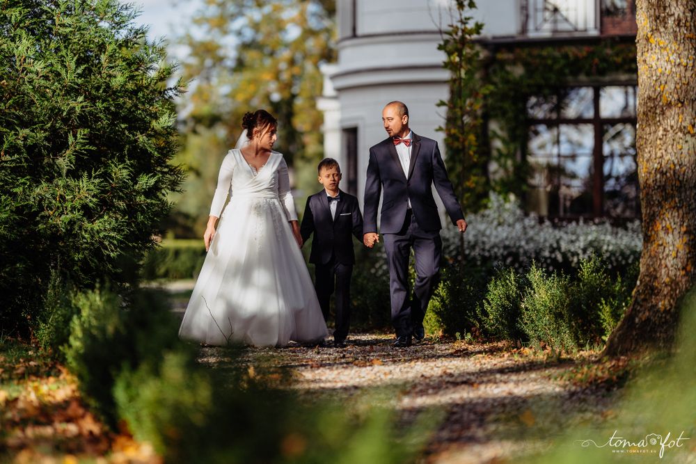 Family walking together down a garden path surrounded by lush greenery on a sunny autumn day.