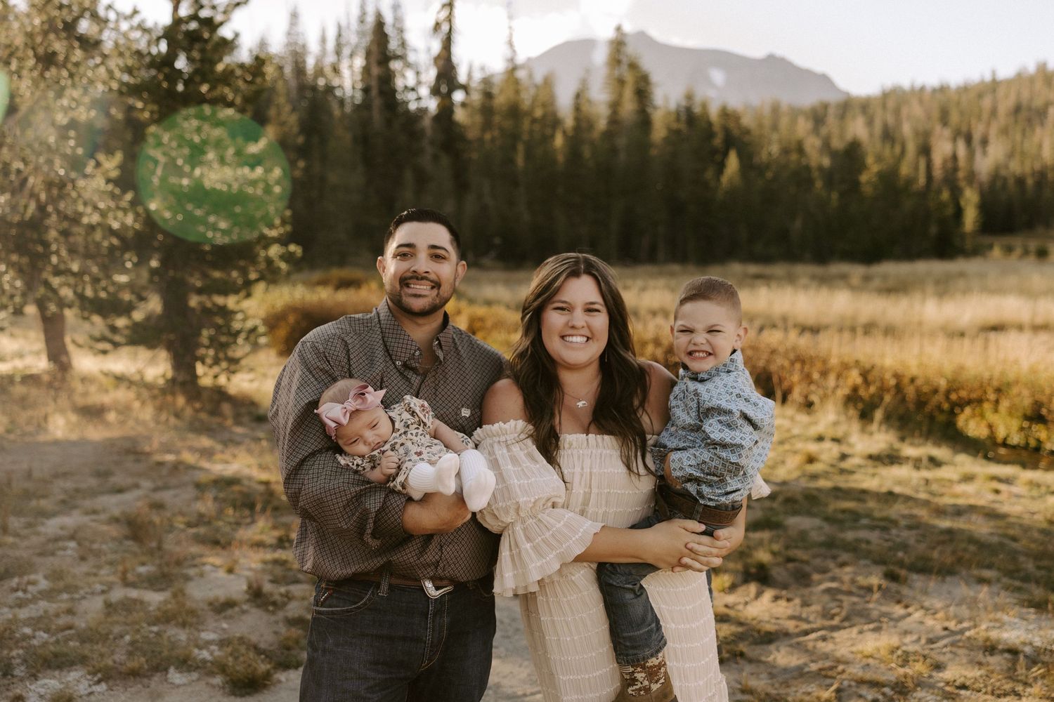 A happy family shares joyful moments together during a golden hour photo session in a mountain meadow setting.