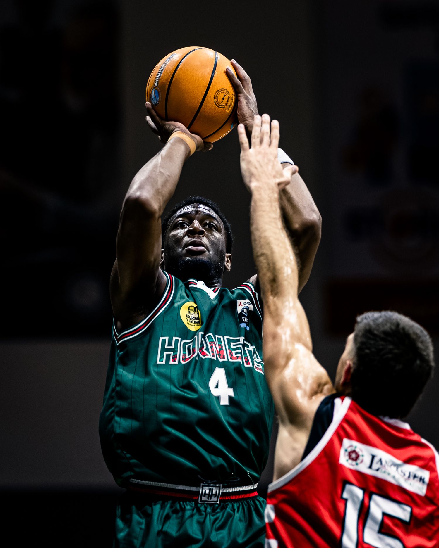 Basketball player in green Hornets jersey attempts shot against defender in red.