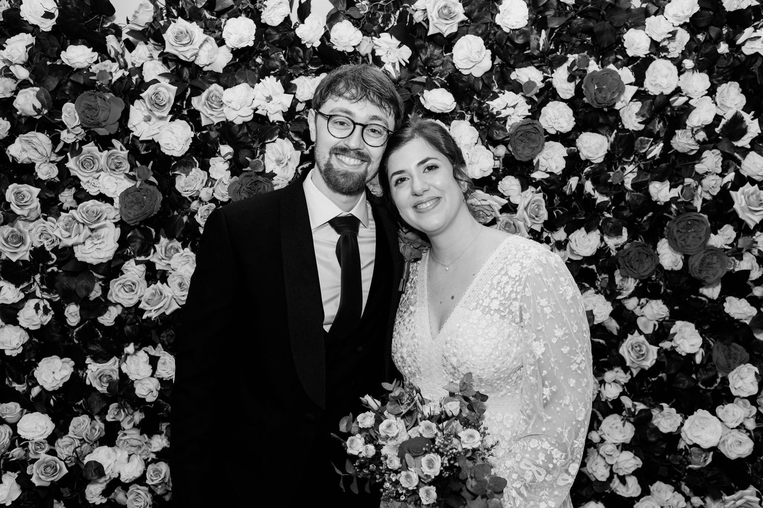 A wedding couple poses against a floral wall backdrop in a series of romantic black and white photographs.