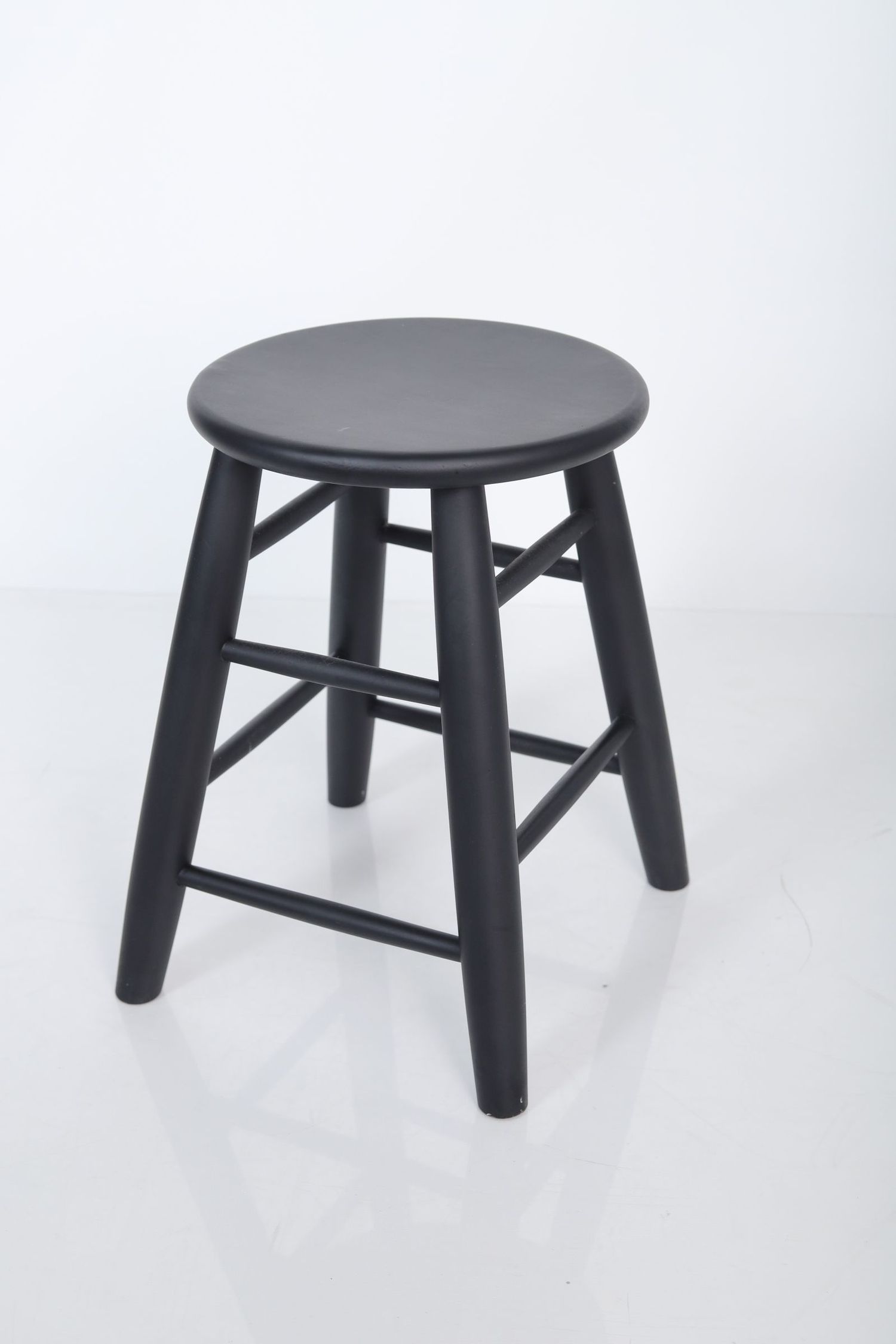 Four identical black wooden stools with round seats and sturdy legs shown from different angles on white background.