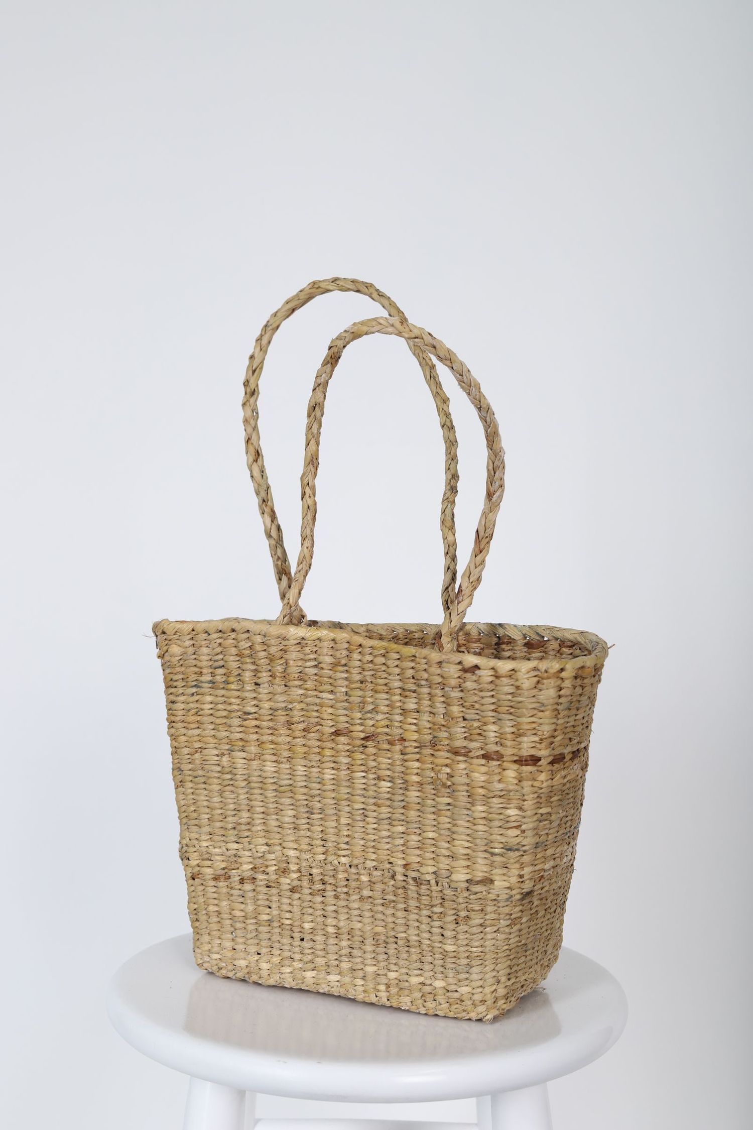 Natural woven seagrass market basket with handles shown from multiple angles on white surface.