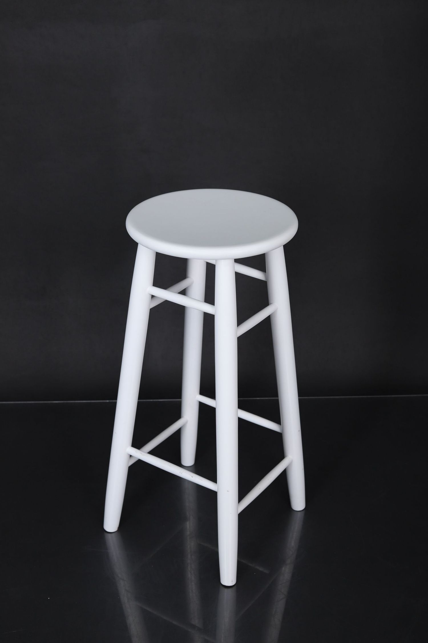 Four identical white wooden stools photographed from different angles against a dark background.