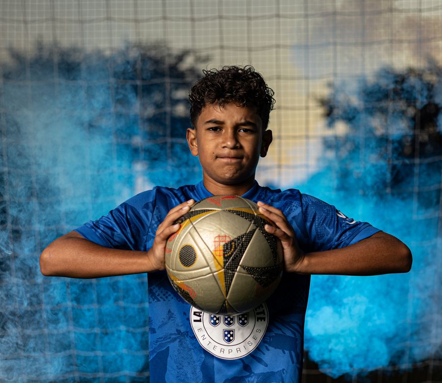 boy flexing a soccer ball in a flex with blue smoke and soccer goal behind him dramatic sports portraits hampton roads virginia