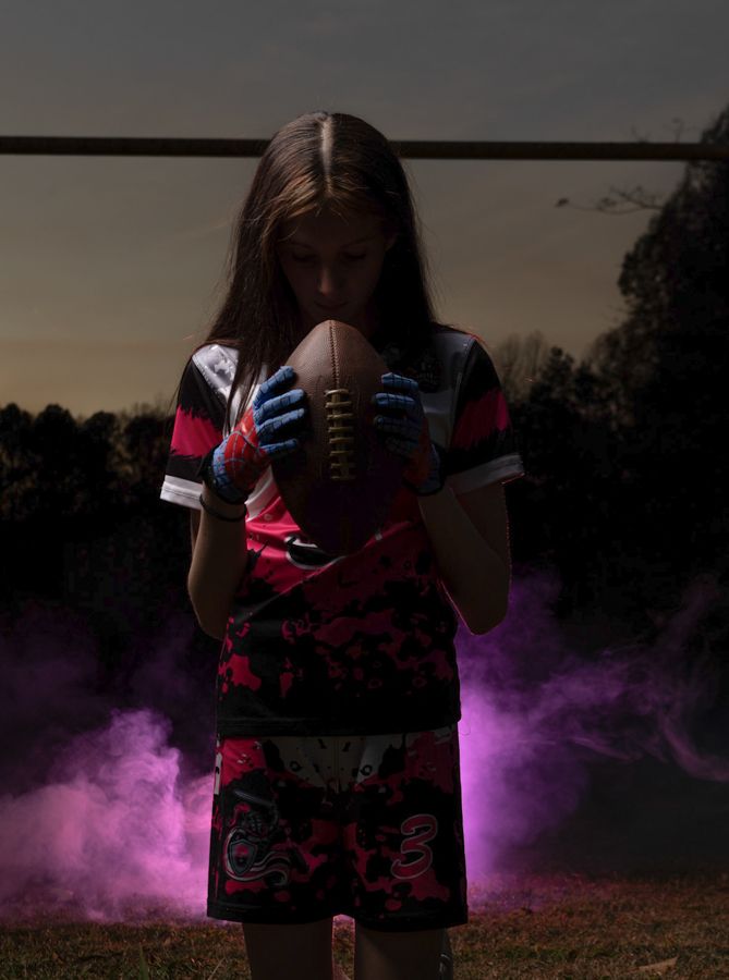 girl flag football player bowing her head over football for a football prayer dramatic sports portraits in gloucester virginia