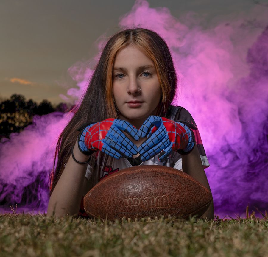 flag football girl making heart hands over a football with pink smoke in the background. Dramatic sports portrait in the hampton roads