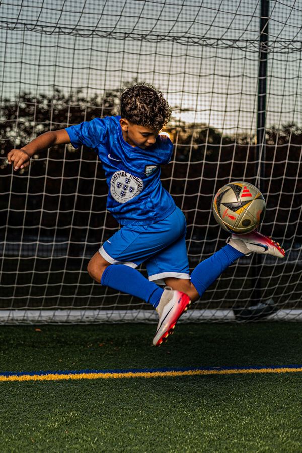 boy soccer player wearing blue sharks uniform in the wisc soccer field in williamsburg virginia kicking the ball up
