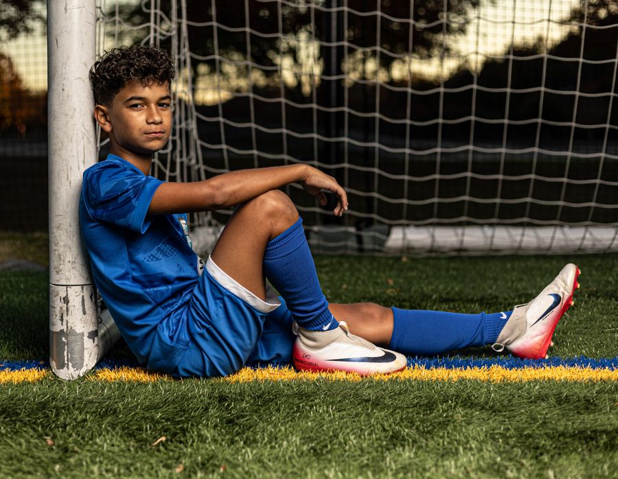 boy soccer player wearing blue sitting in a soccer goal draping his arm across his knee