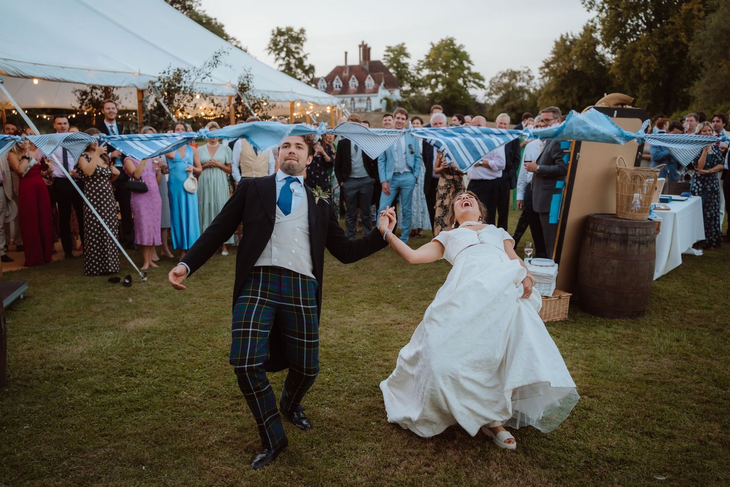 A sequence of candid outdoor wedding reception photos showing guests dancing and celebrating on a grassy lawn at dusk.