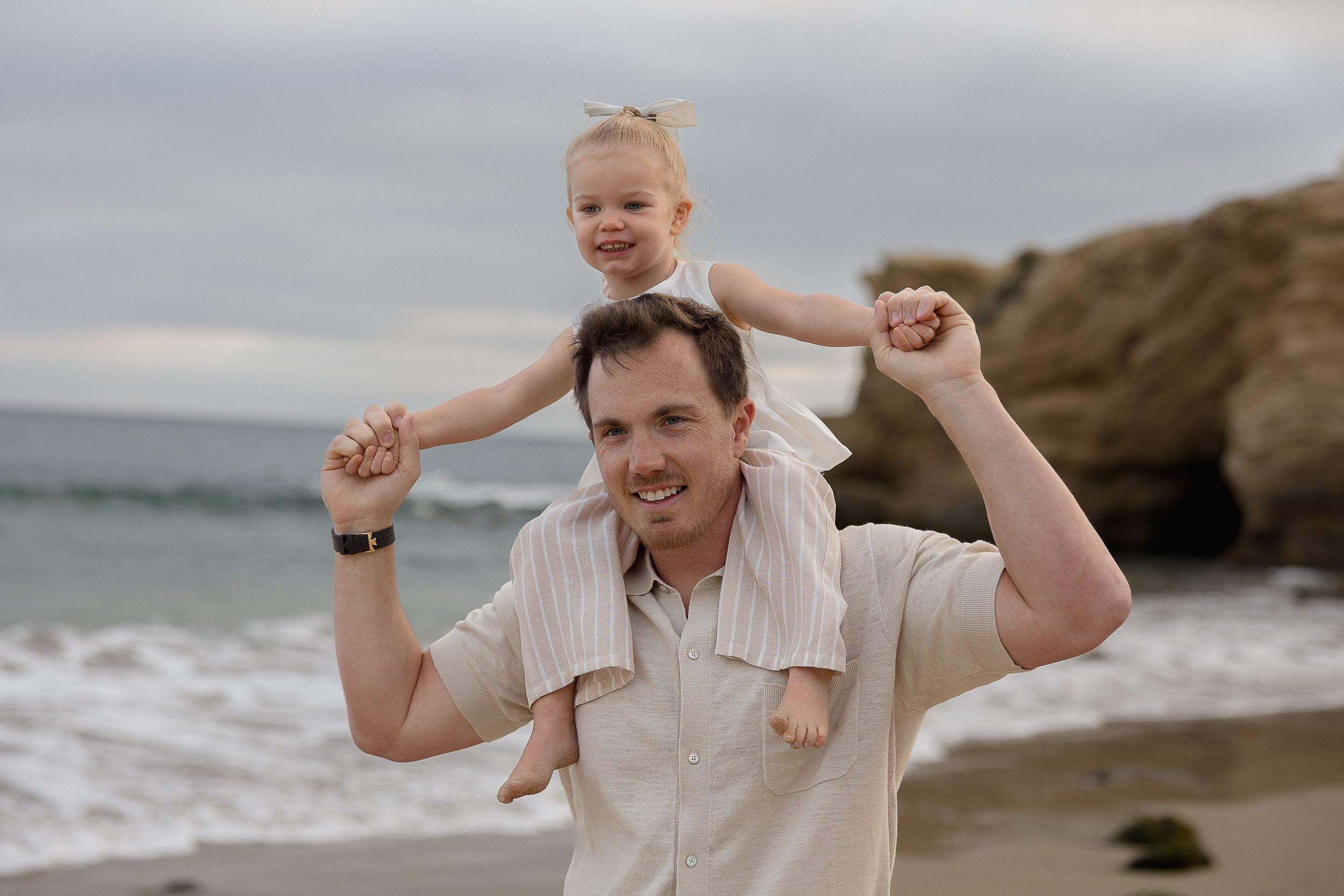 A family enjoys a playful moment together while walking along a scenic coastal beach on a cloudy day.