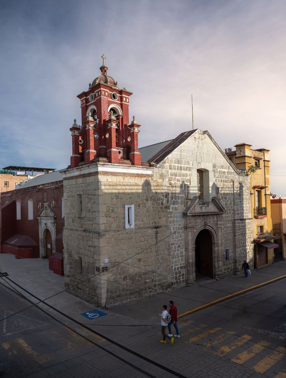 Historic stone church with red bell tower and white walls along a cobblestone street in Arequipa, Peru at sunset.