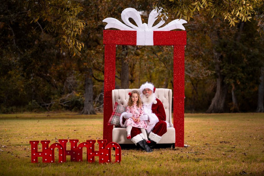 Holiday photo setup with large red gift box frame and decorations in outdoor setting.