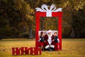 A large red decorative gift box frame with white bow sits on autumn grass with ho-ho-ho letters in the foreground.