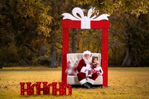 Large red Christmas present photo prop frame setup outdoors with festive decorations in autumn setting.